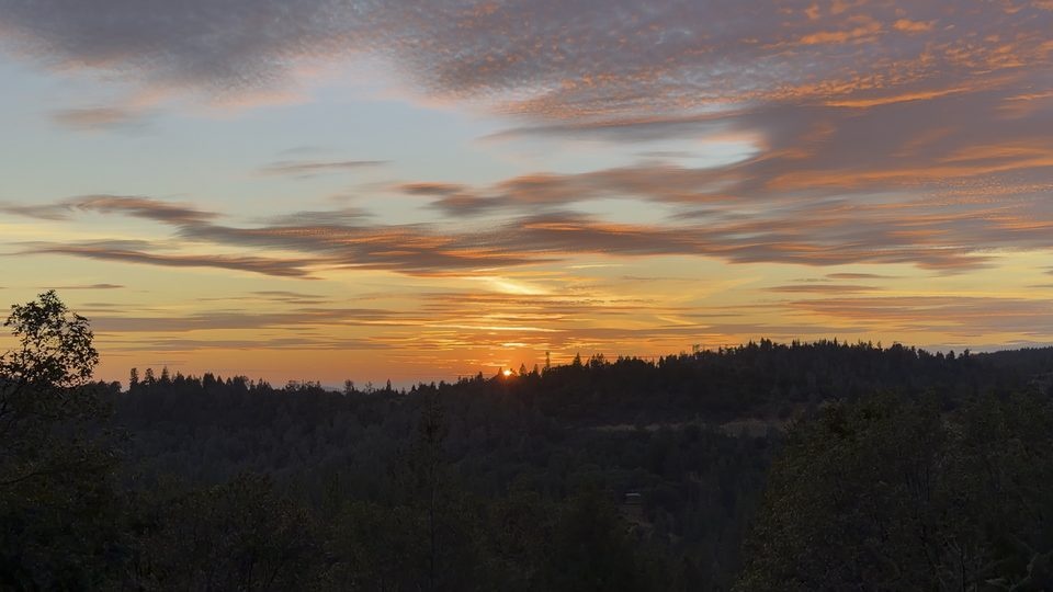 Scattered gold cloud over a dark ridge as the sun sets